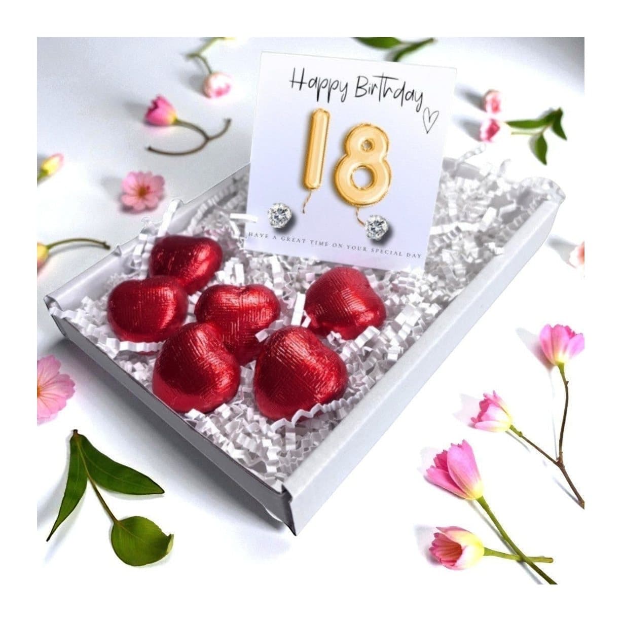 Cubic zirconia stud earrings on a gold balloons card beside red foiled chocolate hearts