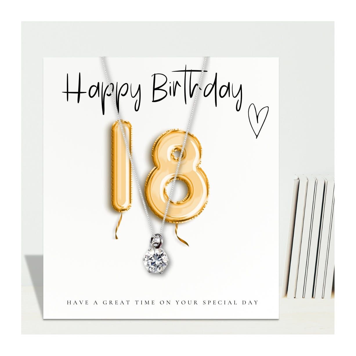 Silver necklace with a cubic zirconia charm beside a gold balloons message card