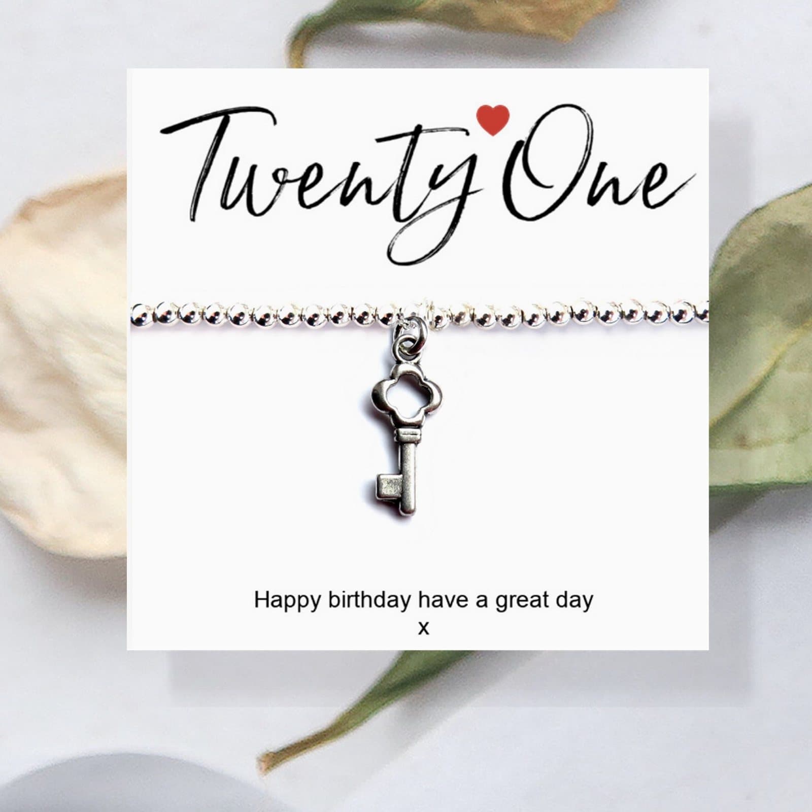 Silver beaded stretch bracelet with a key charm, next to a 21st birthday message card