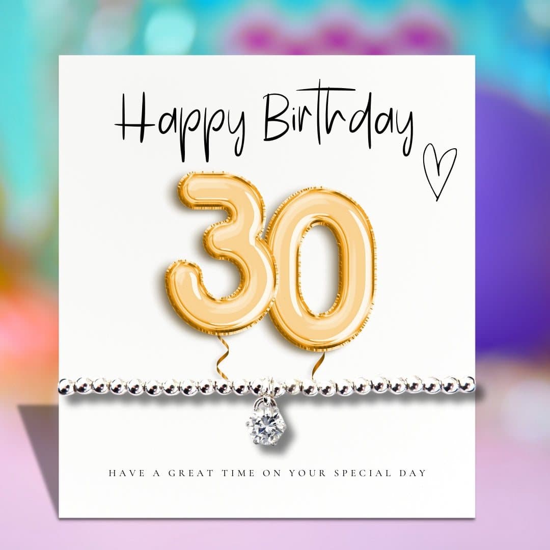 Silver stretch bracelet with a cubic zirconia charm beside a gold balloons card
