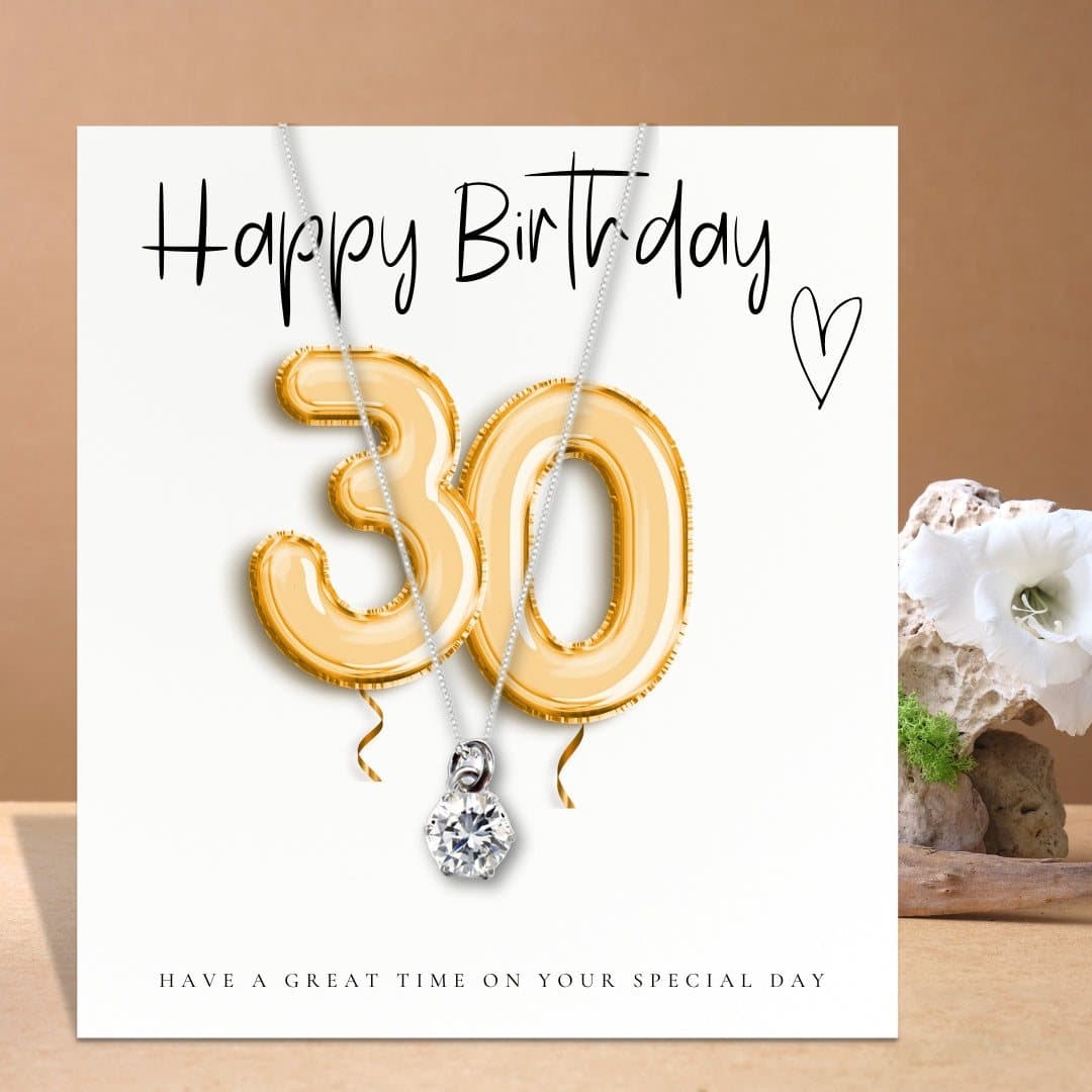 Silver necklace with a cubic zirconia charm beside a gold balloons message card