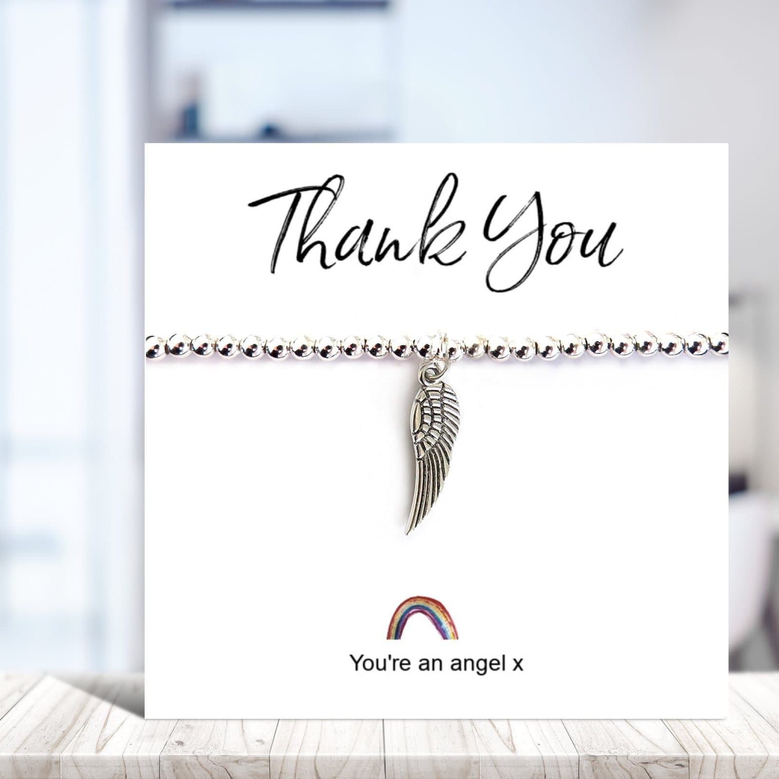 Silver beaded stretch bracelet with an angel wing charm on a rainbow thank you card