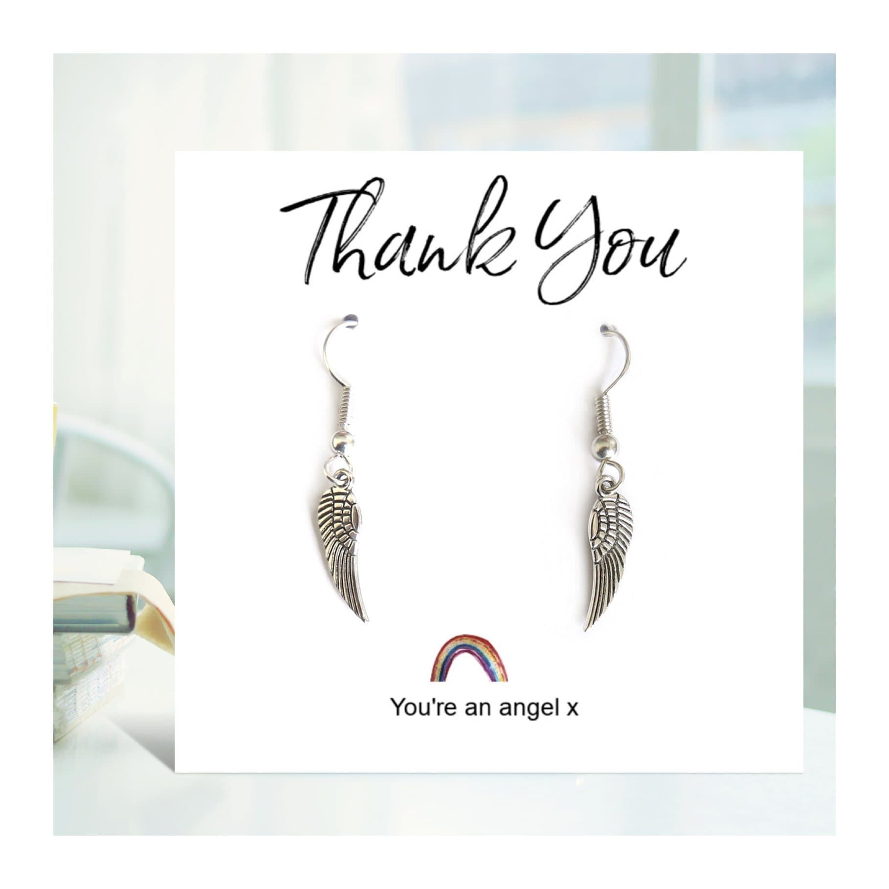 Silver angel wing drop earrings on a rainbow thank you card