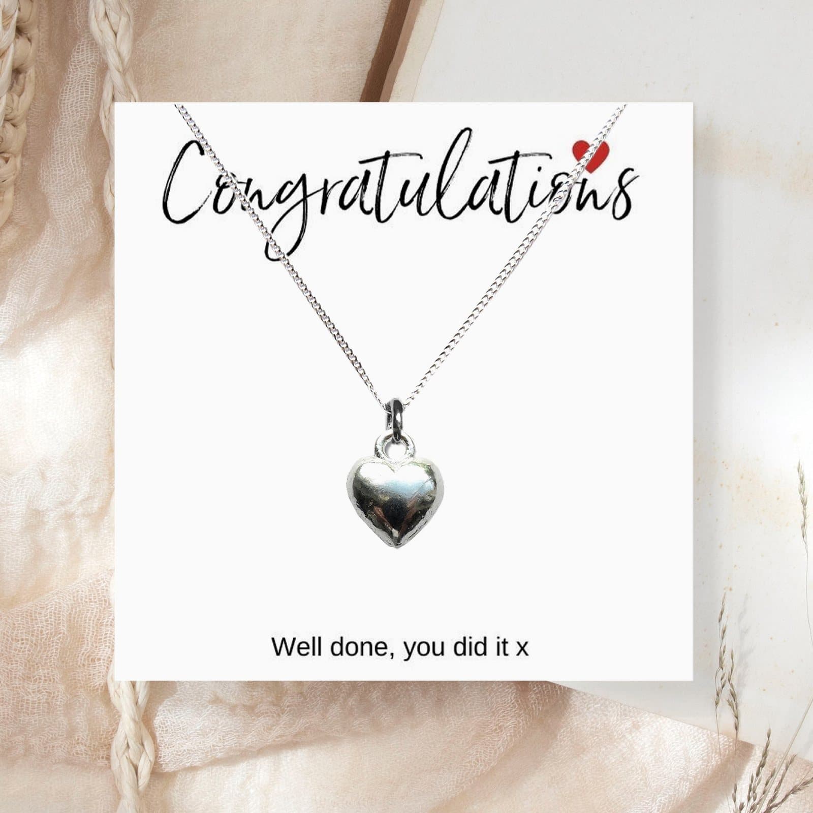 A silver heart charm on a silver chain, with a congratulations message card