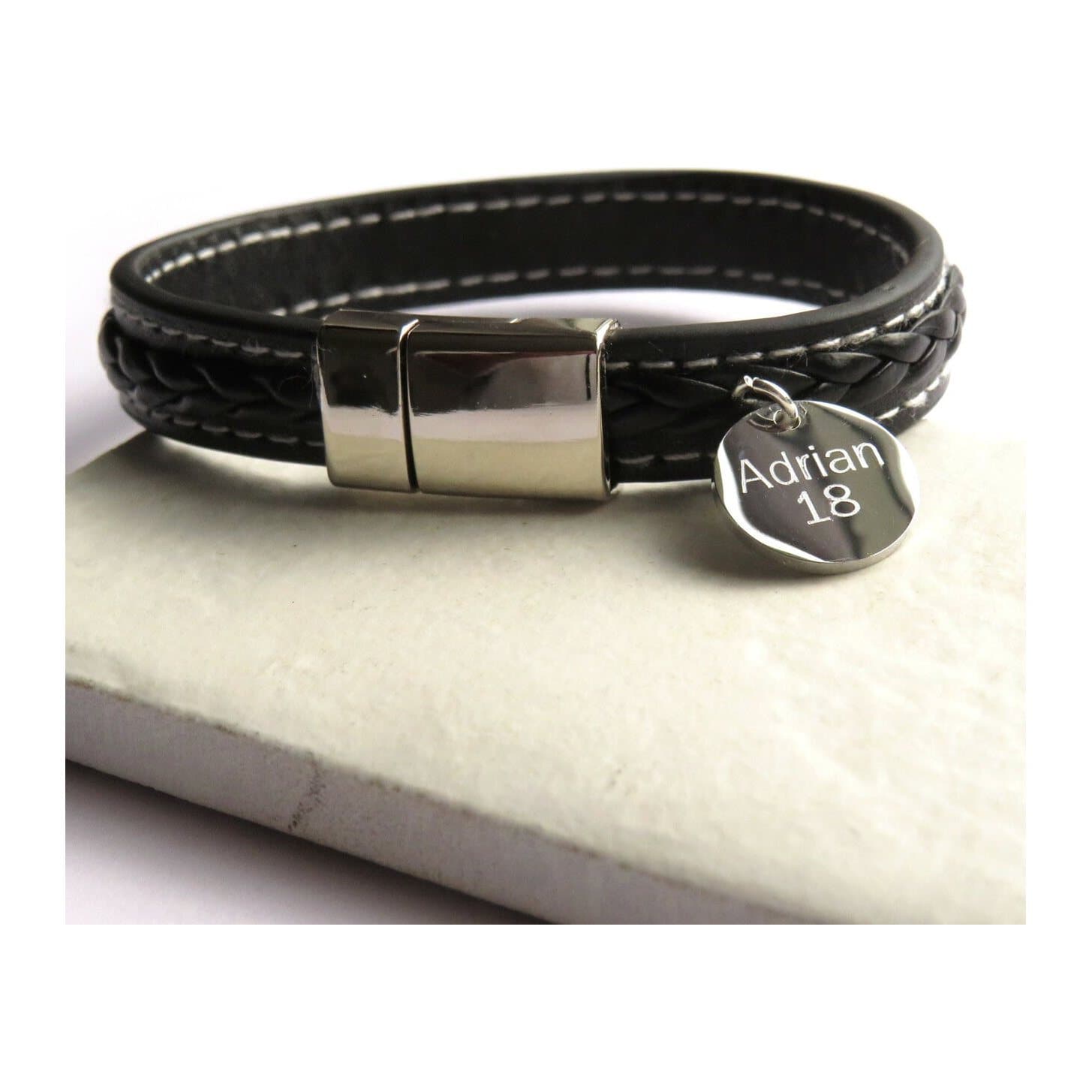 Black faux leather men's bracelet with white stitching and a round steel charm