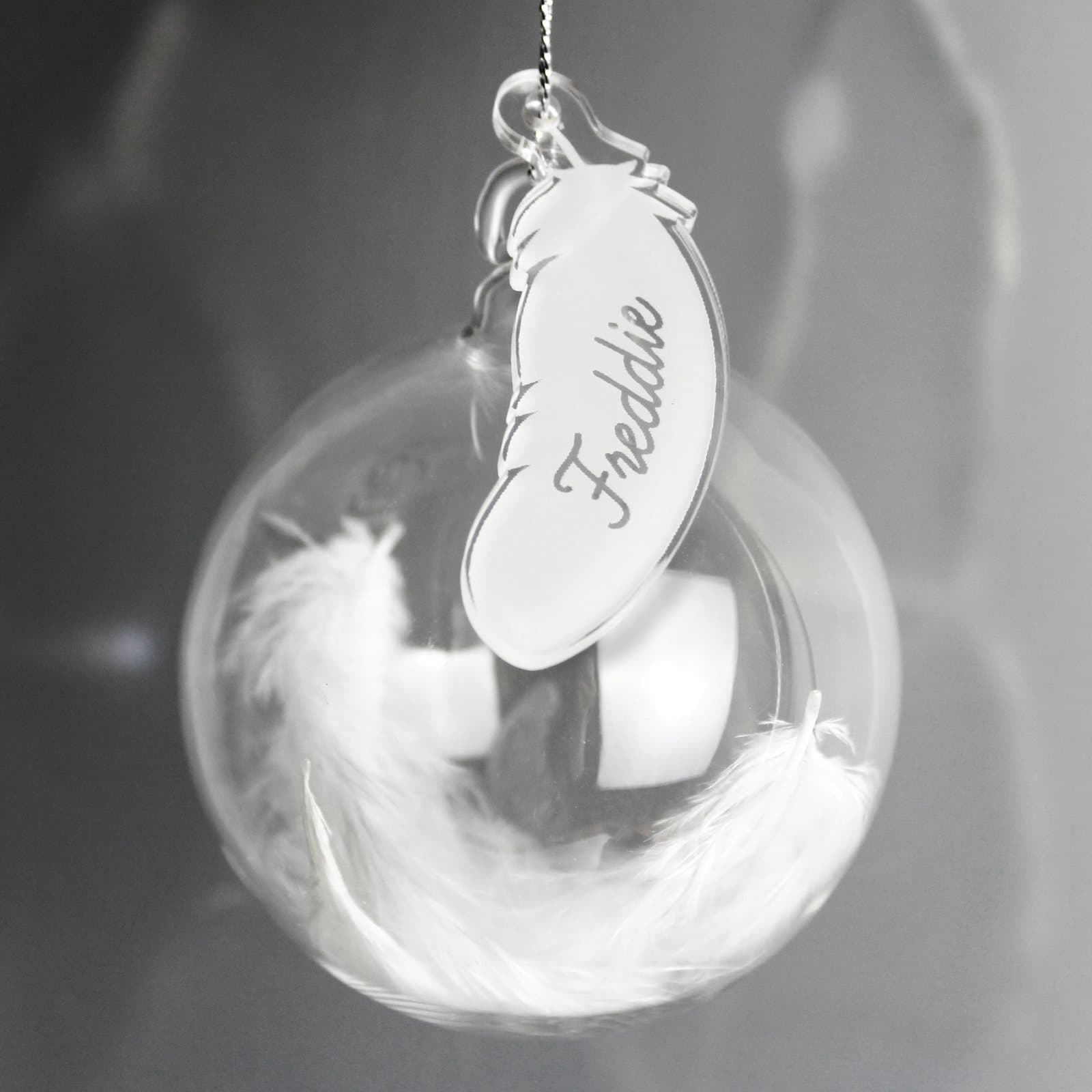 Glass bauble filled with a feather and an acrylic feather tag