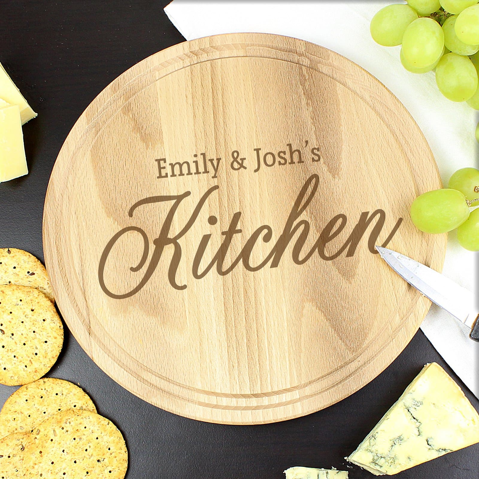 Round natural wood chopping board engraved with two names and the word Kitchen