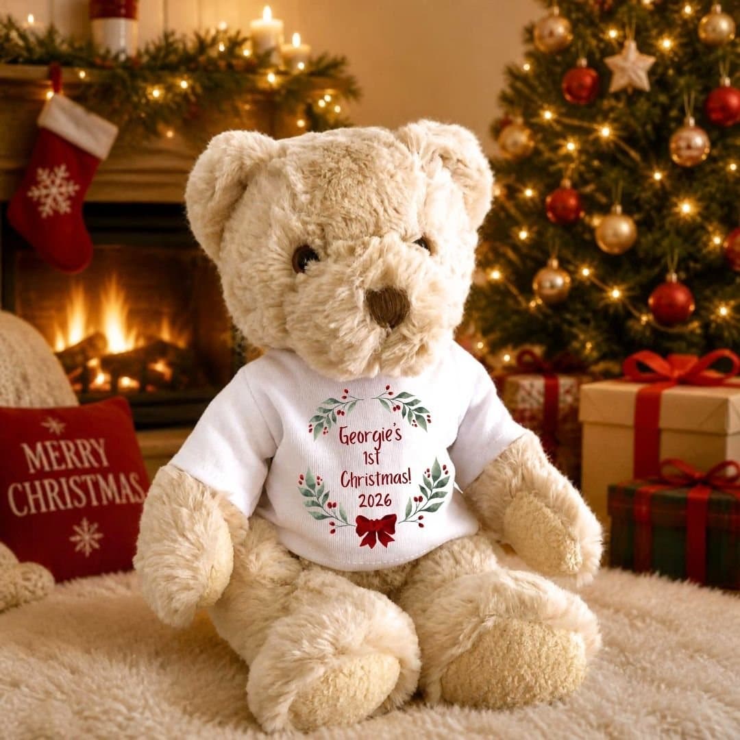 Teddy bear in a T-shirt with holly, berries and a red bow, saying 1st Christmas 2026.