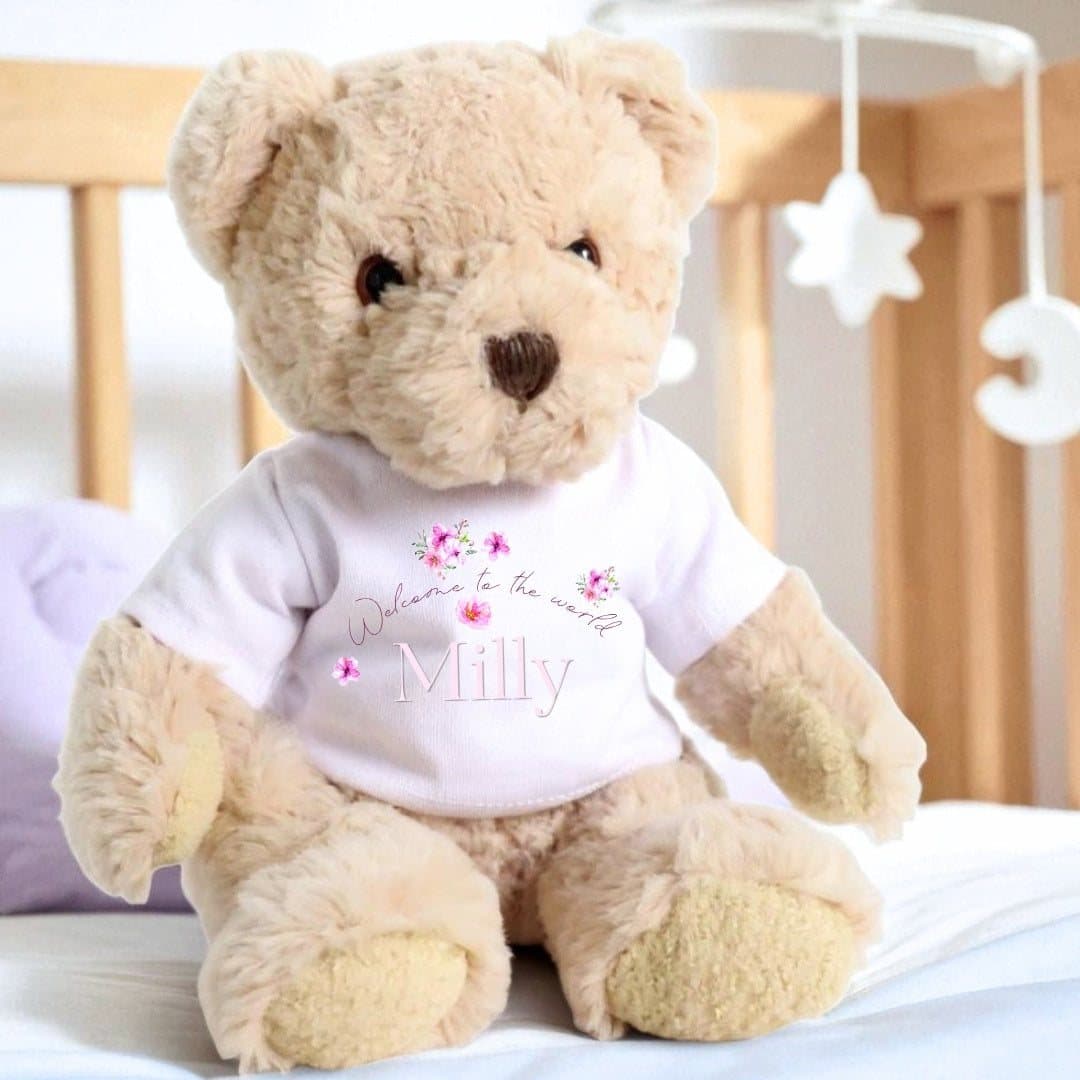 Teddy bear wearing a T-shirt printed with Welcome to the World and floating flowers
