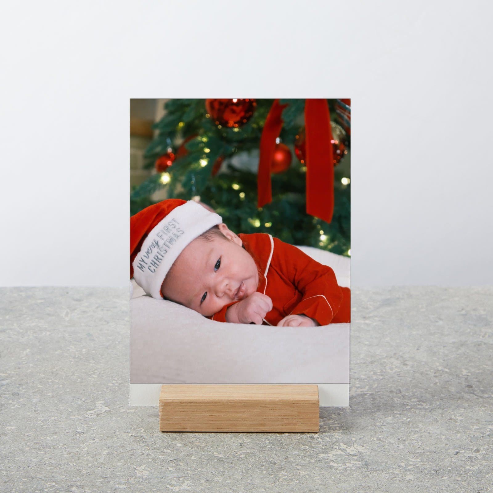 Photo of a baby in a Santa hat standing in a small oak stand